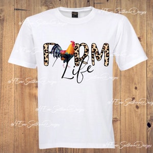 May include: White t-shirt featuring the text "FARM LIFE" with a colorful rooster graphic. The word "FARM" has a leopard print design. The shirt is a crew neck and has short sleeves.