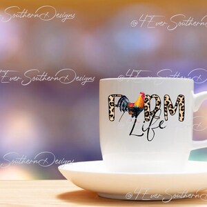 May include: A white ceramic mug and saucer set. The mug features the words "FARM LIFE" with a rooster illustration. The letters "FARM" have a leopard print design. The background is blurred with shades of purple and yellow.
