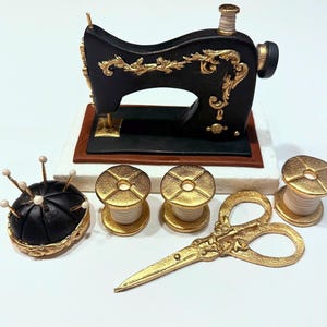 May include: A black and gold vintage sewing machine cake topper with a pincushion, two spools of thread, and a pair of gold scissors.