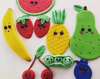 May include: A set of ten colorful, hand-painted, fondant fruit and vegetable decorations. The set includes a banana, two strawberries, a watermelon slice, a pineapple, a pear, a pea pod with three peas, two cherries, and a blueberry. Each fruit and vegetable has a cute cartoon face.