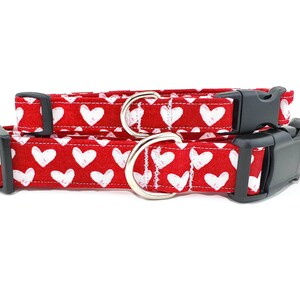 May include: Two red dog collars with white hearts printed on them. The smaller collar is 5/8 inch wide and the larger collar is 1 inch wide. Both collars have black plastic buckles.