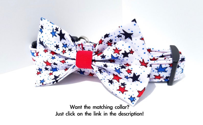 May include: A white dog collar with a red, white, and blue star print bow tie. The bow tie is made of fabric and has a red center. The collar is adjustable and has a black buckle.
