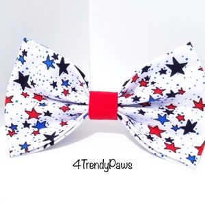 May include: A white bow tie with a red, blue, and black star pattern. The bow tie has a red band in the center. The text "4TrendyPaws" is printed below the bow tie.
