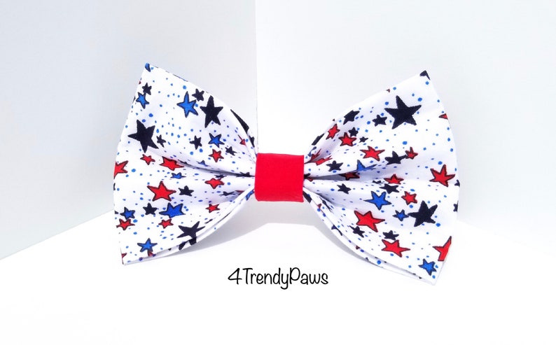 May include: A white bow tie with a red, blue, and black star pattern. The bow tie has a red band in the center. The text "4TrendyPaws" is printed below the bow tie.