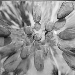 May include: A black and white photo of smooth, oval-shaped stones arranged in a circular pattern on a reflective surface.