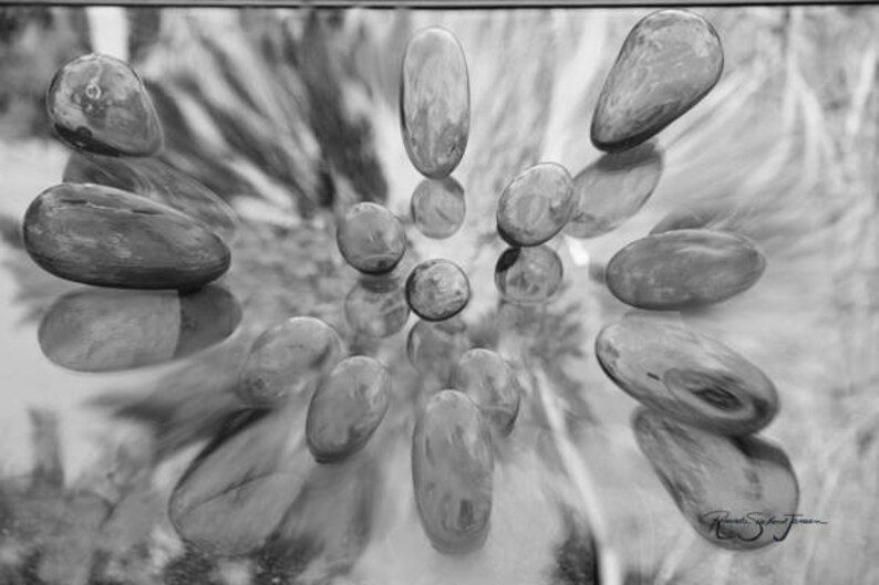 May include: A black and white photo of smooth, oval-shaped stones arranged in a circular pattern on a reflective surface.