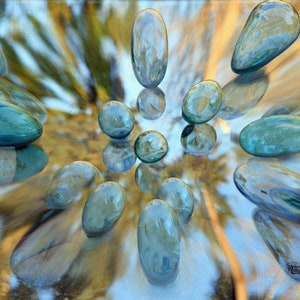 May include: A collection of blue and green glass stones arranged in a circular pattern on a light brown background.