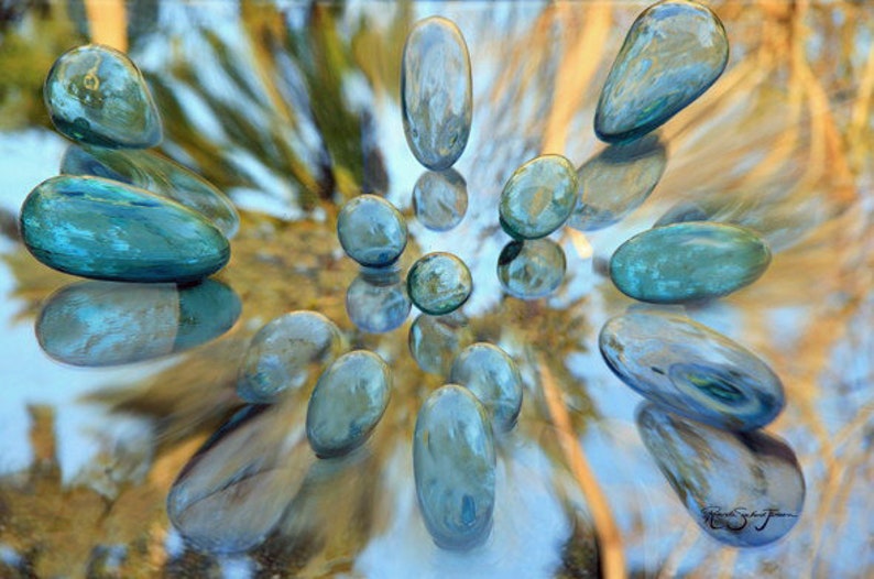 May include: A collection of blue and green glass stones arranged in a circular pattern on a light brown background.