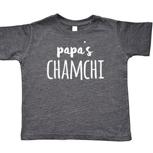 May include: A dark gray t-shirt with the text "papa's chamchi" printed in white.
