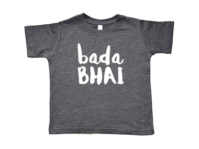 May include: A dark gray t-shirt with the words "bada BHAI" printed in white, a casual top for children. The shirt has short sleeves and a crew neck, suitable for everyday wear.