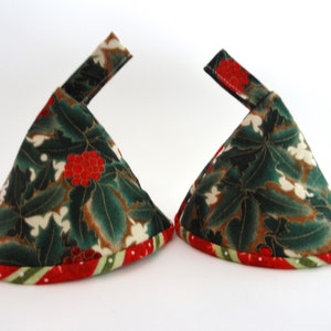 May include: Two Christmas-themed fabric items. Each has a conical shape with a green holly and red berry pattern. The base is trimmed with a red and green striped fabric. A small, rectangular fabric piece extends from the top of each item.
