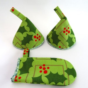 May include: A set of three green and red Christmas-themed pot holders and a matching oven mitt. The items feature a holly leaf pattern with red berries and a light green and blue patterned trim. Each pot holder has a small loop.