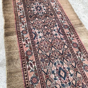 Puede incluir: Una alfombra persa vintage de corredor con fondo marr&oacute;n y intrincados patrones florales y geom&eacute;tricos en tonos rosa, azul y negro.
