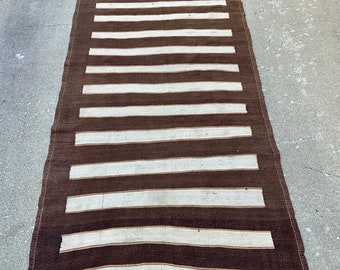 Puede incluir: Una alfombra larga de rayas marrones y blancas con textura tejida. La alfombra tiene un diseño sencillo con rayas marrones y blancas alternas.