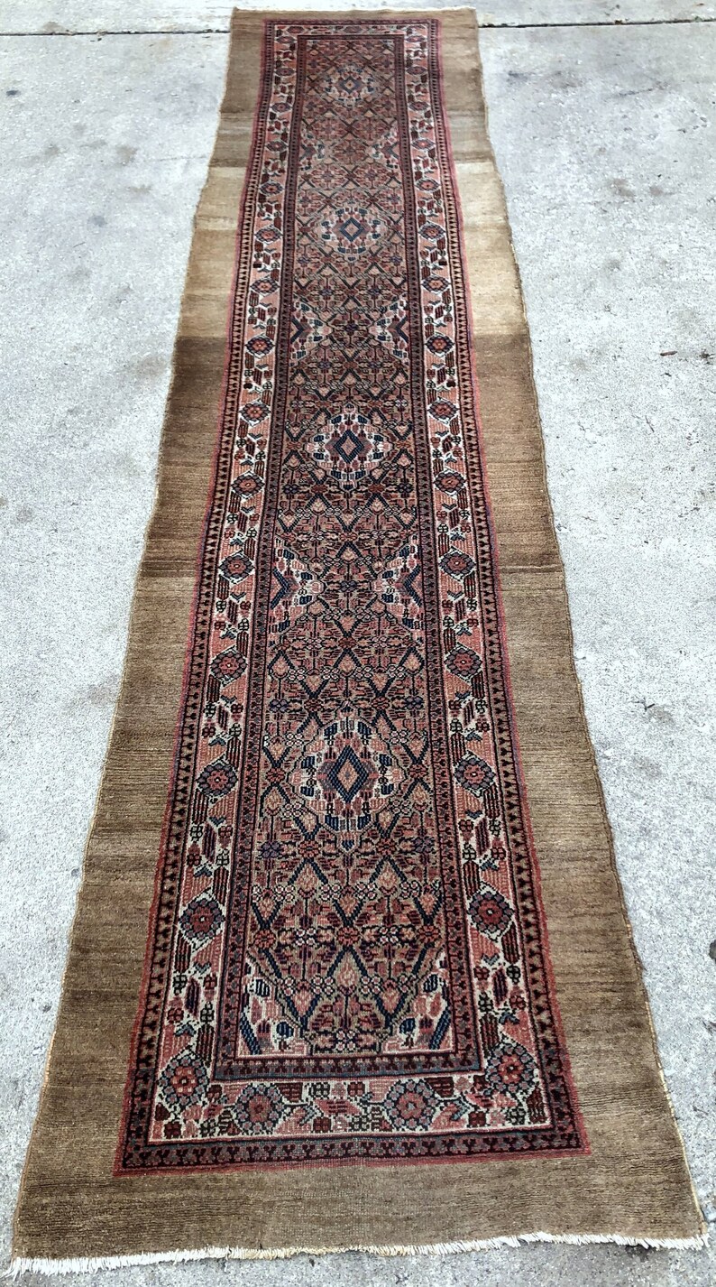 Puede incluir: Una alfombra larga y estrecha con un dise&ntilde;o persa tradicional. La alfombra tiene un fondo marr&oacute;n con un patr&oacute;n rojo, azul y blanco. La alfombra est&aacute; flecos en todos los lados.