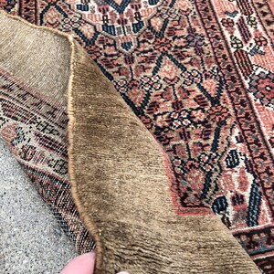 Puede incluir: Un primer plano del reverso de una alfombra con una textura marr&oacute;n tejida. El lado frontal de la alfombra es visible, mostrando un patr&oacute;n floral colorido con tonos de rosa, azul y blanco.