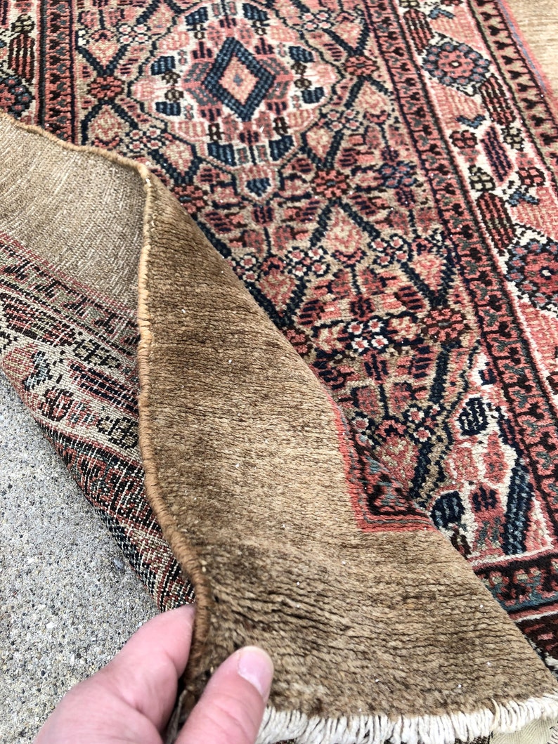 Puede incluir: Un primer plano del reverso de una alfombra con una textura marr&oacute;n tejida. El lado frontal de la alfombra es visible, mostrando un patr&oacute;n floral colorido con tonos de rosa, azul y blanco.
