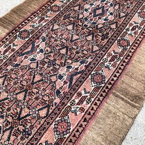 Puede incluir: Una alfombra larga y estrecha con un dise&ntilde;o persa tradicional. La alfombra tiene un borde marr&oacute;n y un centro rosa y azul con intrincados patrones geom&eacute;tricos.