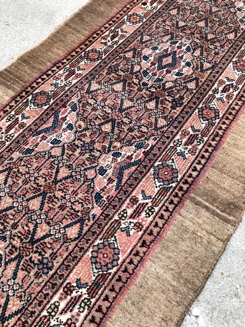 Puede incluir: Una alfombra larga y estrecha con un dise&ntilde;o persa tradicional. La alfombra tiene un borde marr&oacute;n y un centro rosa y azul con intrincados patrones geom&eacute;tricos.