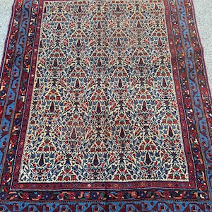 May include: A traditional Persian rug with a cream-colored background and a repeating floral pattern in shades of red, blue, and green. The rug has a wide border with intricate geometric designs.