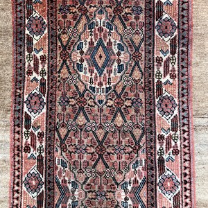 Puede incluir: Una alfombra vintage con un patr&oacute;n geom&eacute;trico detallado en tonos de rosa, azul y marr&oacute;n. La alfombra tiene un medall&oacute;n central y un borde con motivos florales.