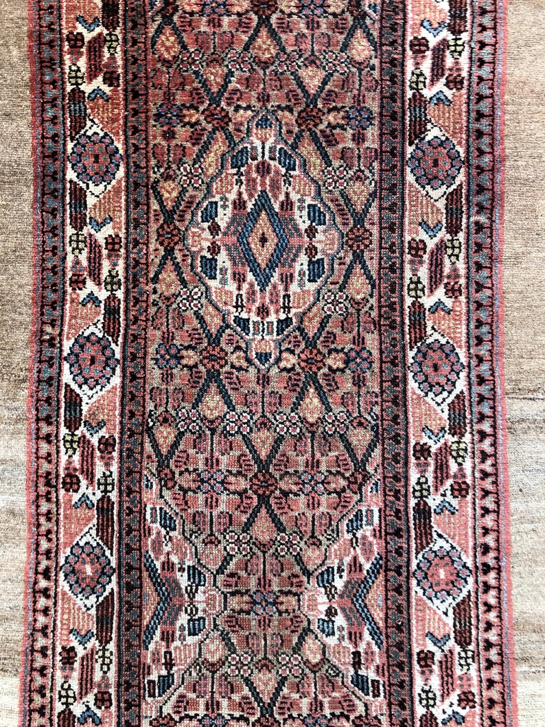 Puede incluir: Una alfombra vintage con un patr&oacute;n geom&eacute;trico detallado en tonos de rosa, azul y marr&oacute;n. La alfombra tiene un medall&oacute;n central y un borde con motivos florales.