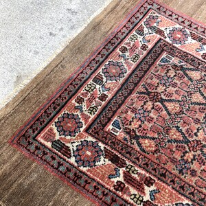 Puede incluir: Una alfombra vintage con fondo marr&oacute;n y un dise&ntilde;o estampado en rojo, azul y blanco. La alfombra tiene un borde con flecos.