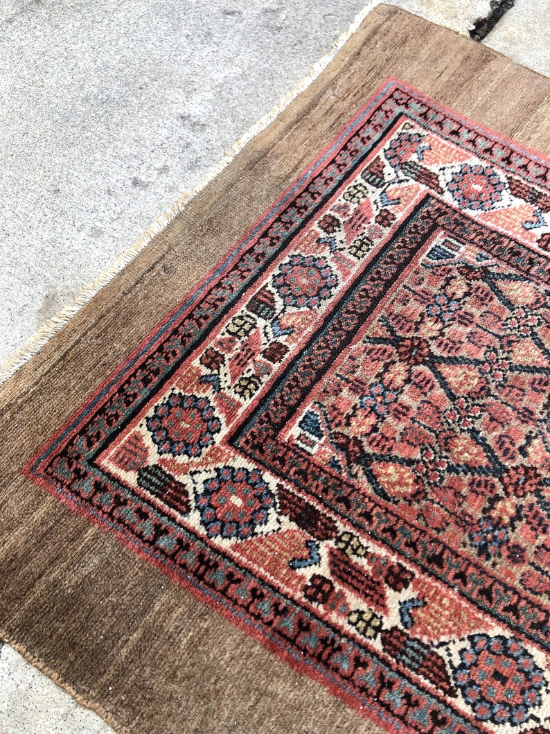 Puede incluir: Una alfombra vintage con fondo marr&oacute;n y un dise&ntilde;o estampado en rojo, azul y blanco. La alfombra tiene un borde con flecos.