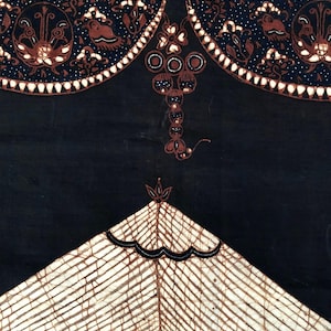 Op de afbeelding: Een zwarte stof met een wit en bruin batik-ontwerp. Het ontwerp heeft een geometrisch patroon met een centrale driehoekvorm en een decoratieve rand.