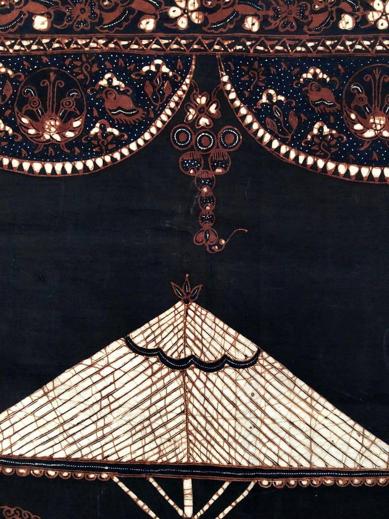 Op de afbeelding: Een zwarte stof met een wit en bruin batik-ontwerp. Het ontwerp heeft een geometrisch patroon met een centrale driehoekvorm en een decoratieve rand.