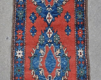 Puede incluir: Una alfombra roja, azul y blanca con un diseño tradicional. La alfombra tiene un borde marrón y está hecha de lana.