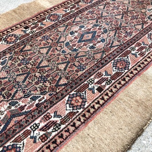 Puede incluir: Una alfombra persa vintage de corredor con un patr&oacute;n geom&eacute;trico tradicional en tonos rojos, azules y beige. La alfombra tiene un borde de flecos y est&aacute; hecha de lana.