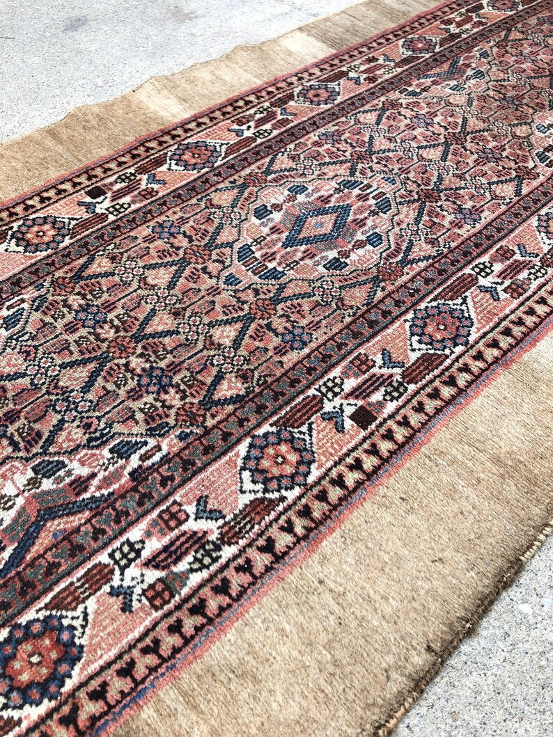 Puede incluir: Una alfombra persa vintage de corredor con un patr&oacute;n geom&eacute;trico tradicional en tonos rojos, azules y beige. La alfombra tiene un borde de flecos y est&aacute; hecha de lana.