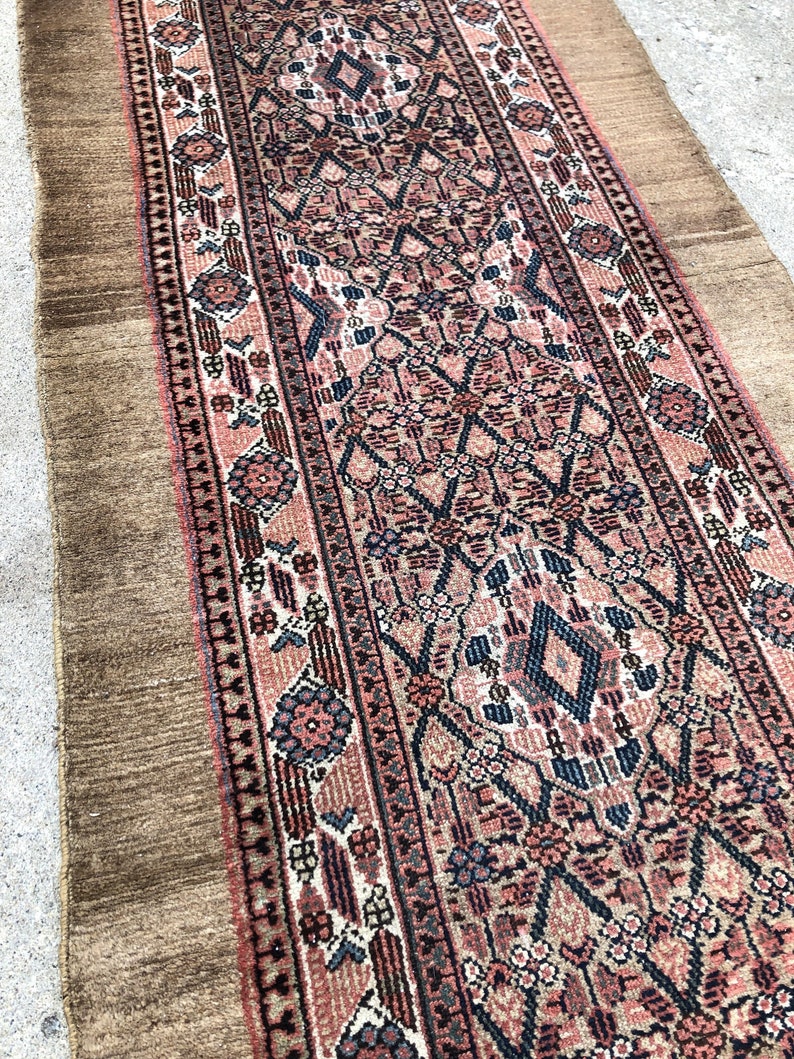 Puede incluir: Una alfombra persa vintage de corredor con fondo marr&oacute;n y intrincados patrones florales y geom&eacute;tricos en tonos rosa, azul y negro.