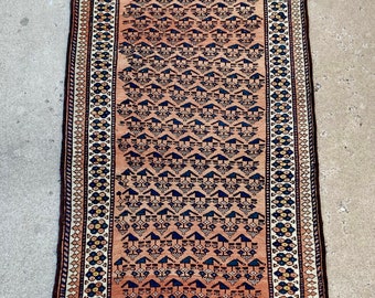 Puede incluir: Una alfombra larga y estrecha con un diseño persa tradicional. La alfombra tiene un fondo marrón con un patrón repetitivo de formas geométricas azules y blancas. El borde de la alfombra es un diseño floral multicolor.