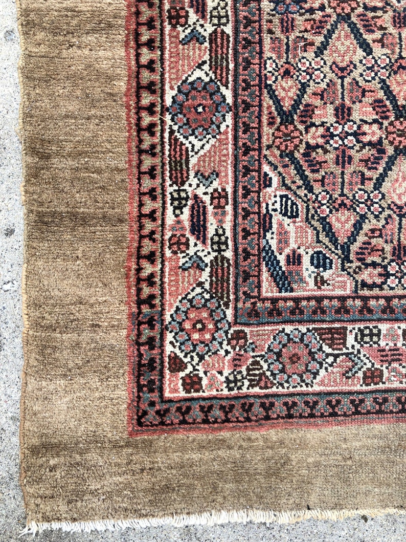 Puede incluir: Primer plano de una alfombra de color marr&oacute;n y rojo con un borde de flecos. La alfombra tiene un dise&ntilde;o floral con detalles intrincados.