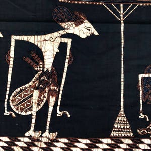 Op de afbeelding: Een zwart-witte batikstof met een traditioneel Indonesisch poppenontwerp. De pop houdt een schild vast en staat onder een witte paraplu. De stof heeft een bruin-witte rand.