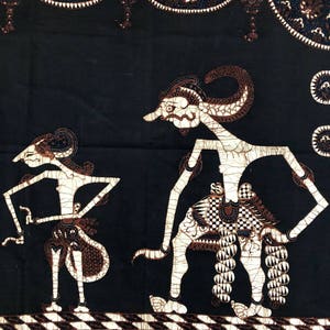 Op de afbeelding: Zwart-witte batikstof met een traditioneel Indonesisch ontwerp met twee figuren met ingewikkelde details. De figuren staan op een gepatroneerde achtergrond.