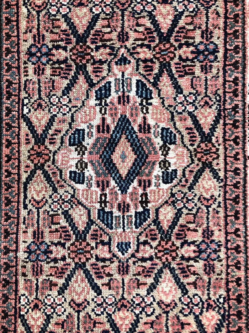 Puede incluir: Una alfombra vintage con un patr&oacute;n geom&eacute;trico rosa, azul y negro. La alfombra tiene una forma de diamante central con intrincados dise&ntilde;os florales.
