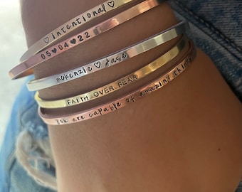 May include: A set of four silver, gold, and copper bracelets with engraved messages. The messages are "♡intentional 05 04 22", "makenzie ♡ Jase", "FAITH OVER FEAR", and "You are capable of amazing things".