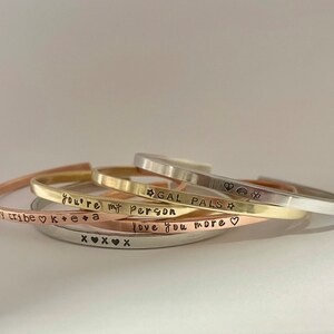 May include: A set of four gold, silver, and copper bracelets with different engraved messages. The messages include "my tribe", "you're my person", "gal pals", and "love you more".
