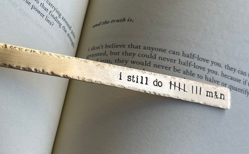 May include: A silver bookmark with the text "i still do" and tally marks. The bookmark is on a page of a book with text about love.