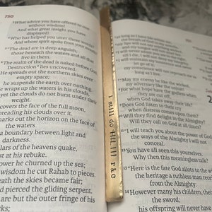 May include: A gold bookmark with the words "I still do" and "R & C" engraved on it. The bookmark is placed on a page of a book with text about the book of Job in the Bible.