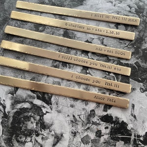 May include: Six silver metal strips with different engraved messages. The messages include "I still do", "8 chapters in", "n&k est 2004", "I still choose you", "I choose you", and "Amor Fati".