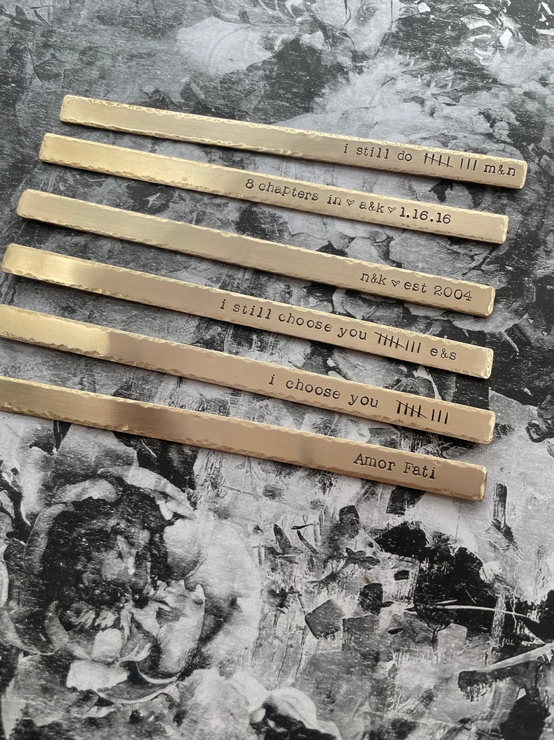 May include: Six silver metal strips with different engraved messages. The messages include "I still do", "8 chapters in", "n&k est 2004", "I still choose you", "I choose you", and "Amor Fati".