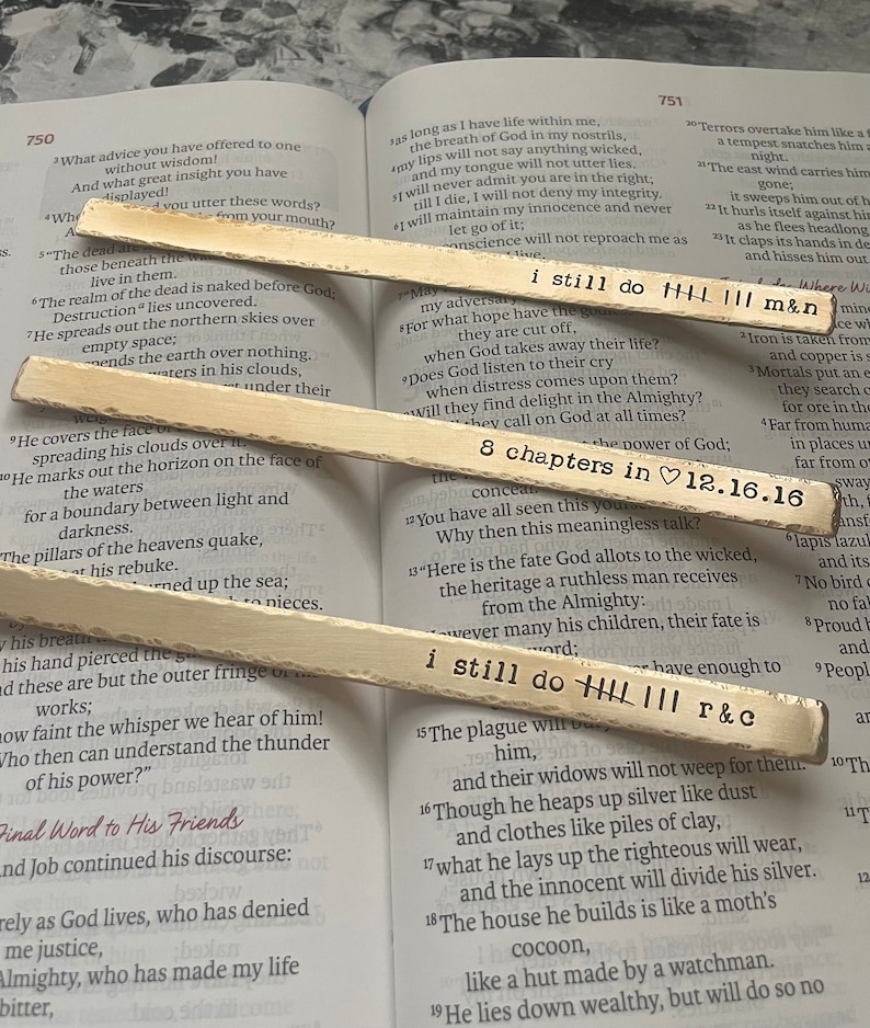 May include: Two wooden sticks with the text "i still do HHH III m&n" and "i still do HHH III r&c" written on them. The sticks are resting on an open book with text about the book of Job from the Bible.