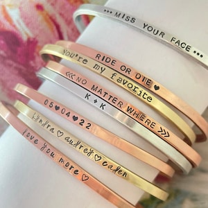 May include: A stack of eight gold, silver, and copper bracelets with various engraved messages, including "Ride or Die", "No Matter Where", "Love You More", and "Miss Your Face".