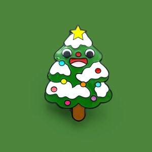 Op de afbeelding: Een groene kerstboom met een witte, met sneeuw bedekte basis en een gele ster bovenop. De boom heeft een glimlachend gezicht met rode wangen en zwarte ogen. De boom is versierd met kleurrijke ornamenten.