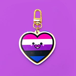 May include: A gold heart-shaped keychain with a smiling face and the colors of the bisexual pride flag. The flag is pink, purple, and blue with a white stripe in the middle.