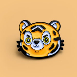 May include: A yellow and black enamel pin featuring a cartoon tiger with a grumpy expression.